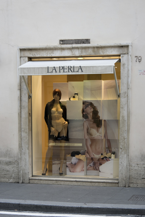 Storefront of a La Perla lingerie shop with a mannequin in beige lingerie and promotional images behind it. Minimal, upscale display with soft lighting.